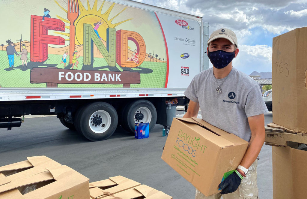 Photo of AmeriCorps member holding a box of food in front of a food bank truck. Image from AmeriCorps.